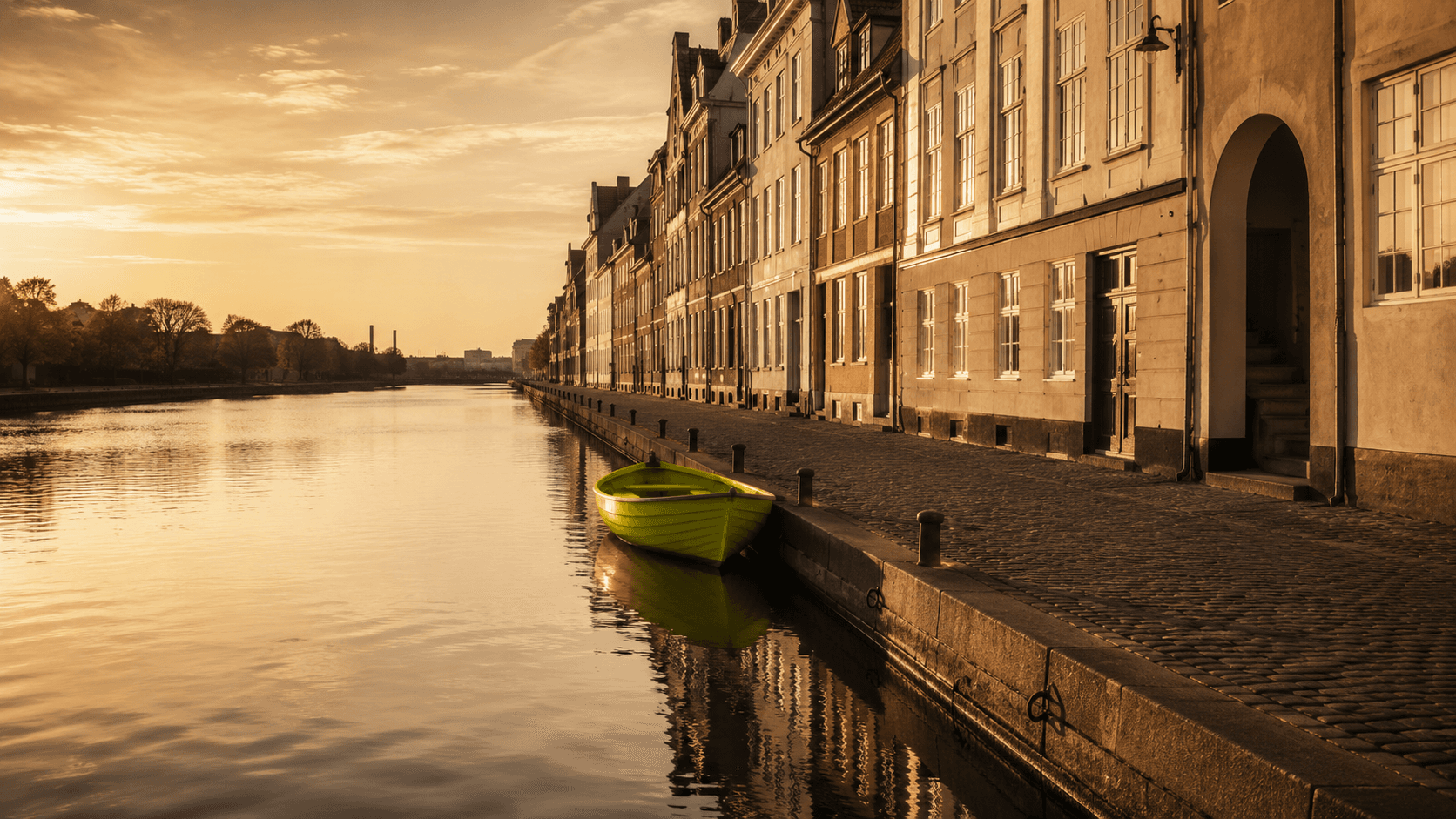 Stille københavnsk kanal i den gyldne time — én chartreusegrøn robåd fortøjet ved den brostensbelagte kaj