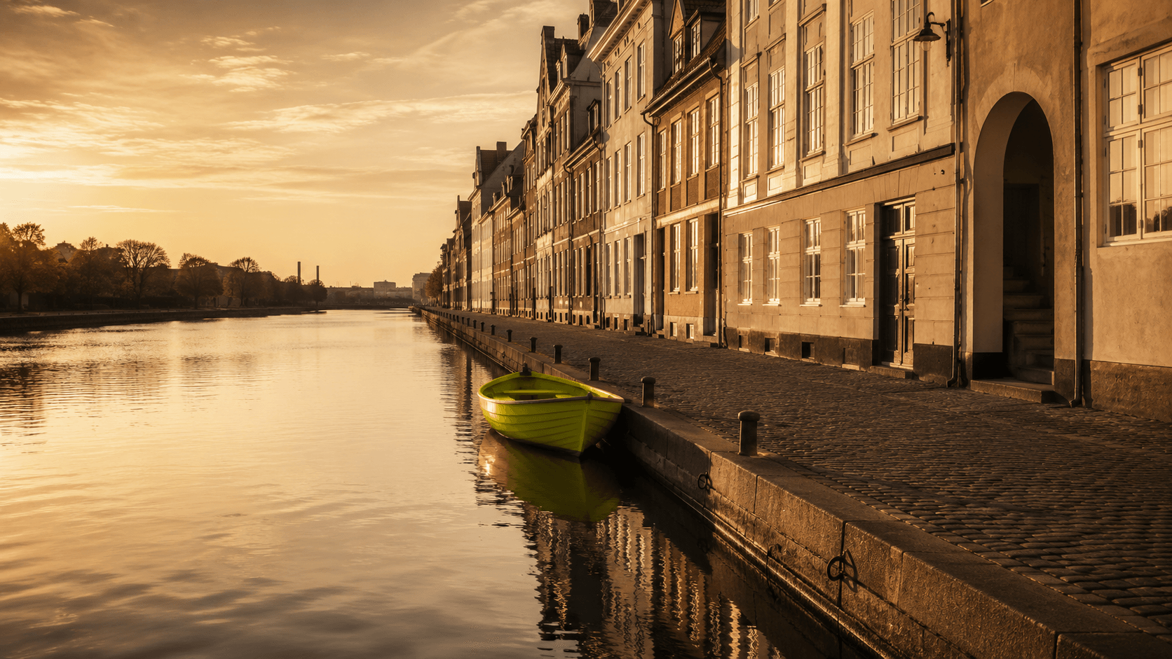 Stille københavnsk kanal i den gyldne time — én chartreusegrøn robåd fortøjet ved den brostensbelagte kaj